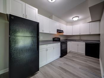 A black fridge in a kitchen with white cabinets.